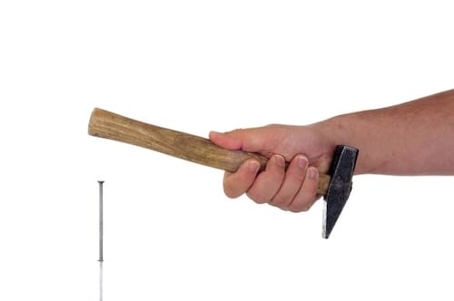 A person trying to use a hammer the wrong way round, with the handle of the hammer striking the nail.